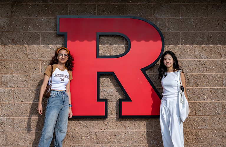 two international students standing in front of rutgers 'R'